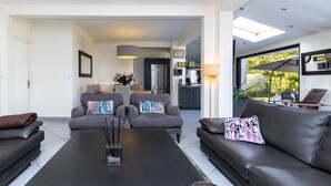 A modern living room with a black coffee table, two grey armchairs, and a black sofa. There is a kitchen in the background with a fridge and a dining area. - Spacious villa on Lake Soustons (Soustons)