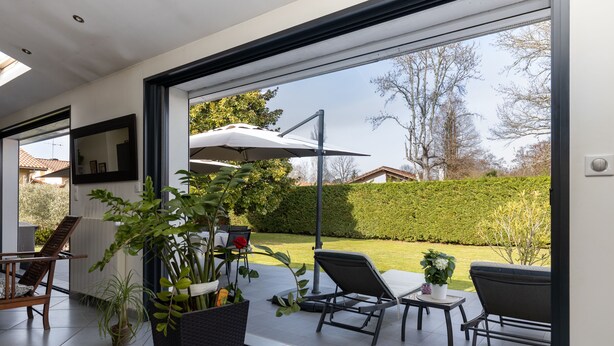 A modern patio with a glass door leading to a garden, featuring outdoor furniture and potted plants. - Spacious villa on Lake Soustons (Soustons)