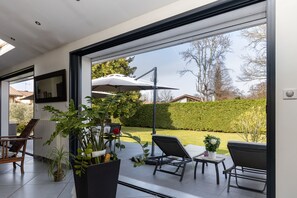 Een modern terras met een glazen deur naar een tuin, met buitenmeubilair en potplanten.