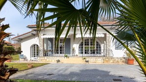 A white building with arched windows and a stone facade, surrounded by greenery and potted plants. - Spacious villa on Lake Soustons (Soustons)