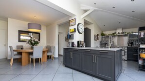 A modern kitchen with grey cabinetry, a central island, and a dining area with a table and chairs. - Spacious villa on Lake Soustons (Soustons)