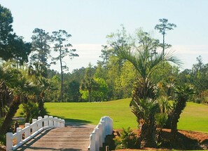 A wooden bridge leading to a golf course with a white fence on one side.
