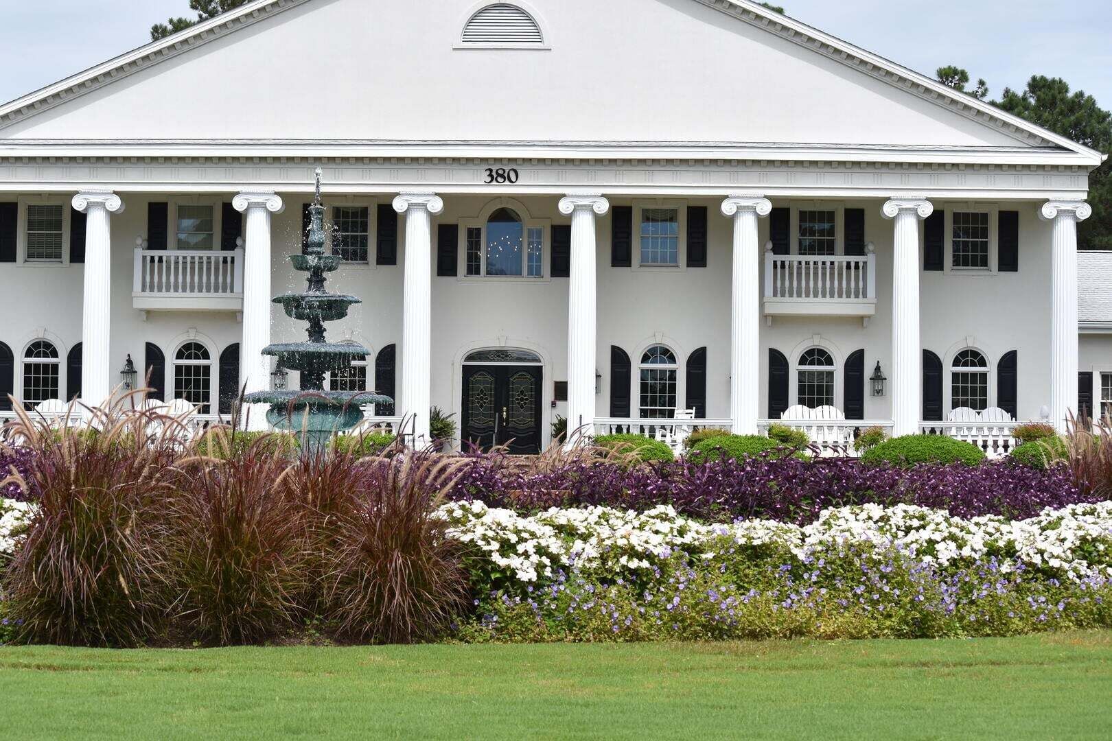 A large white building with a central entrance, columns, and a fountain in the foreground.
