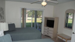 A bedroom with two beds, a TV, a ceiling fan, and a view of a lawn. - Close to Beach Brunswick Plantation Condo 2302M with 27 Hole Golf Course Onsite by RedAwning (Calabash)