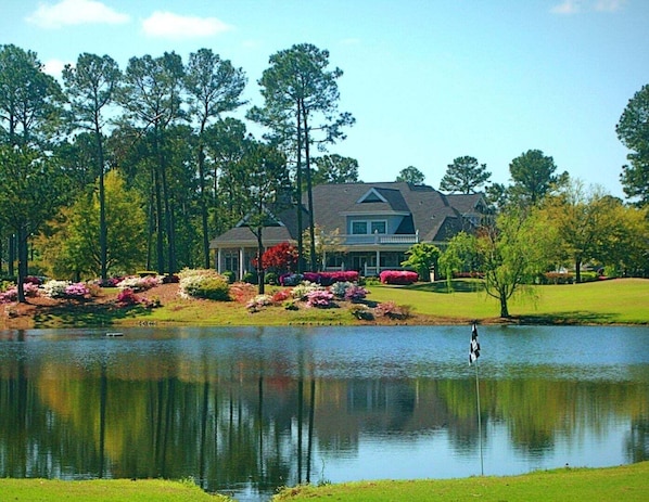 A house with a pond in front, surrounded by trees and landscaped gardens.