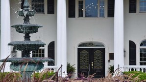A multi-tiered fountain in a garden with a white building featuring a black door and arched windows in the background. - 2302 2 Bedroom Villa by RedAwning (Calabash)