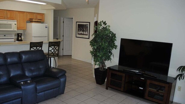 A living room with a black leather sofa, a television on a wooden stand, and a potted plant. - 2302 2 Bedroom Villa by RedAwning (Calabash)