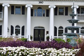 A building with a symmetrical facade, large columns, a central entrance with a black door, and a fountain in the foreground.
