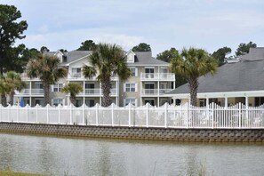 A waterfront hotel with multiple balconies, a white picket fence, and a stone wall.