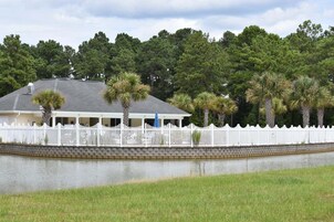 A house with a white picket fence, a covered porch, and a body of water in front.