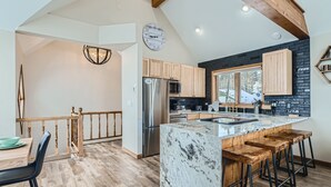 A modern kitchen with wooden cabinets, a stainless steel refrigerator, and a marble island with bar stools. - The Powder Chalet 3 Bedroom Home by RedAwning (Breckenridge)