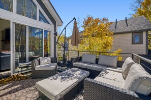 A modern outdoor patio with wicker furniture, a glass door entrance, and a view of a neighboring house. - The Powder Chalet 3 Bedroom Home by RedAwning (Breckenridge)
