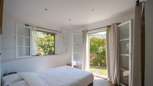 Un dormitorio con una cama, dos ventanas y un ventanal corredera que da a un espacio exterior.