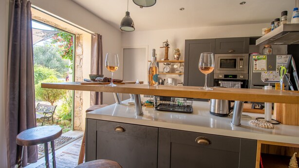 Una cocina moderna con una isla central, luces colgantes y vistas al jardín por la ventana.