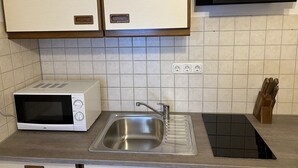 A kitchen with a microwave, sink, and wooden cabinets. - Quiet 1 room apartment (Weilrod)