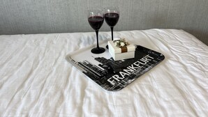 A bed with a white sheet, a tray with a cake and two glasses of red wine, and a wall with a textured pattern. - Quiet 1 room apartment (Weilrod)