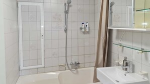 A bathroom with a bathtub, a shower, and a sink. There are toiletries on the wall and a mirror above the sink. - Quiet 1 room apartment (Weilrod)