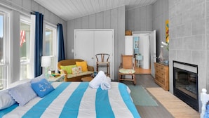 Ein Schlafzimmer mit Bett, Kommode, Sessel, Kamin und einem Fenster mit Vorhängen.
