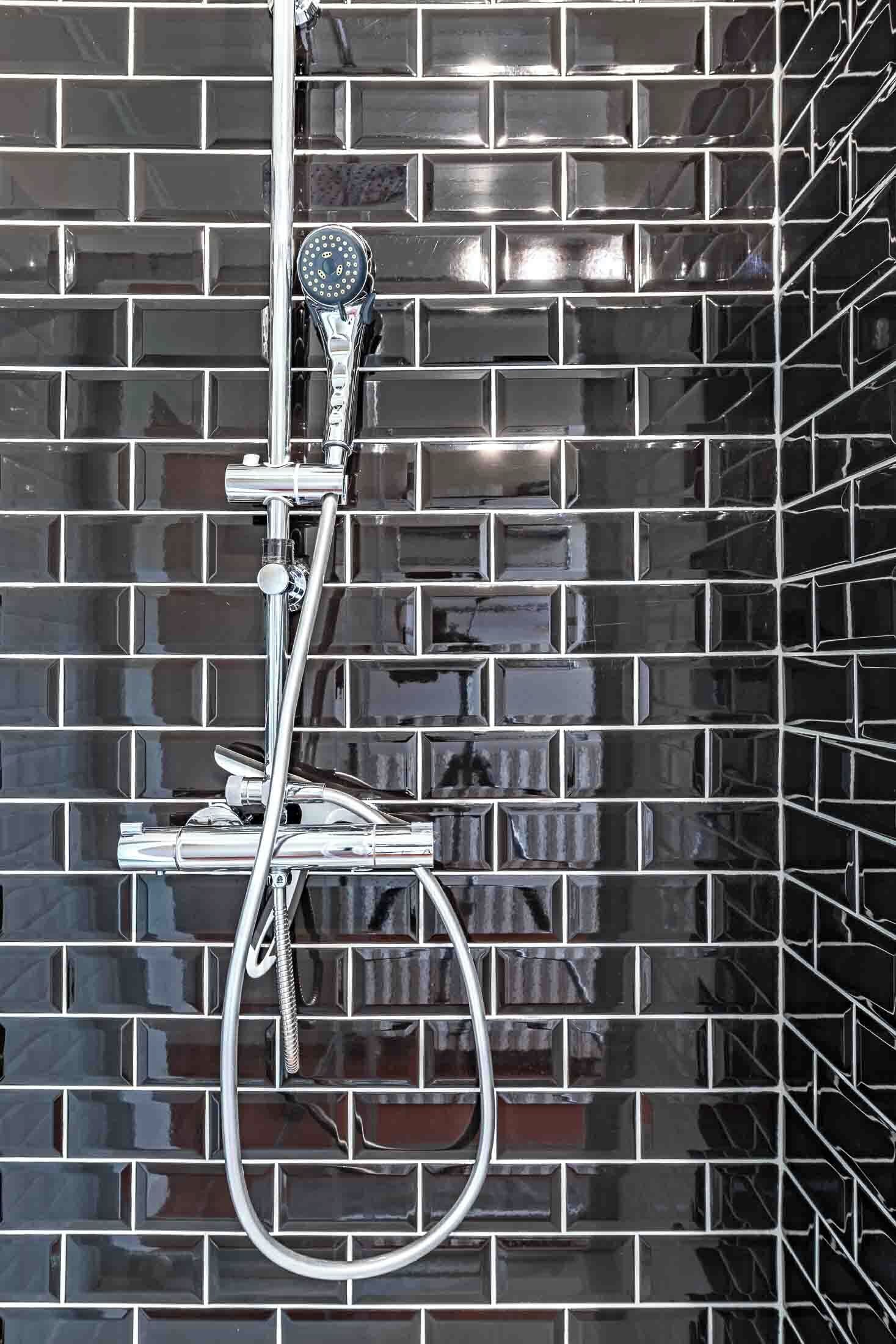 A shower with chrome fixtures against a tiled wall.