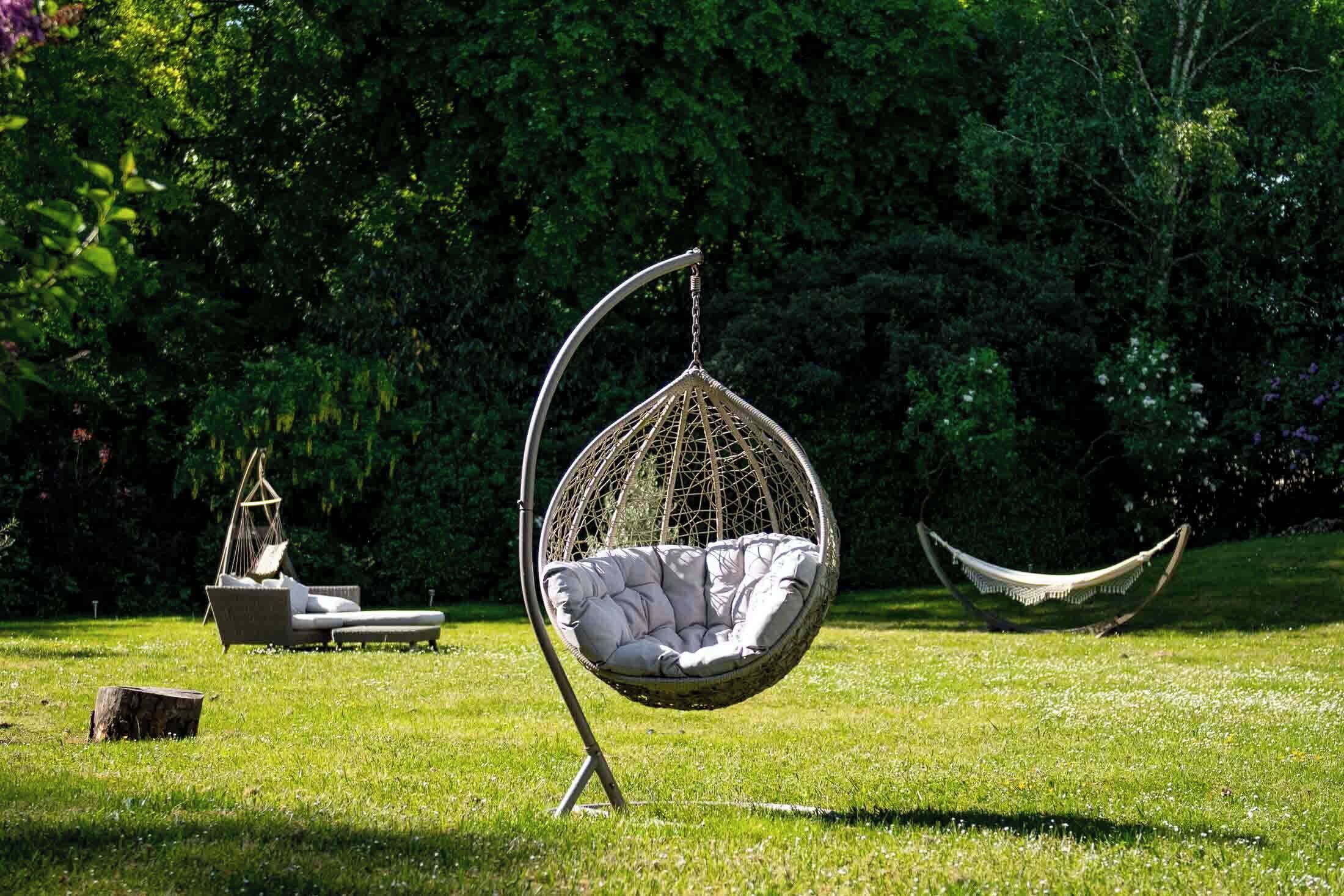 Een hangstoel in een grasrijke omgeving, met een hangmat en een loungestoel op de achtergrond.