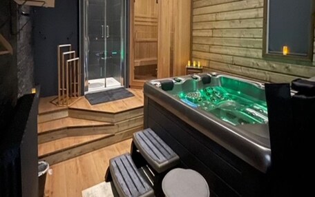 A modern spa room with a wooden wall, a glass-enclosed shower, a hot tub, and wooden steps leading to the shower.