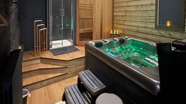 Un spa moderno con pared de madera, ducha envuelta en cristal, bañera de hidromasaje y escalones de madera que conducen a la ducha.