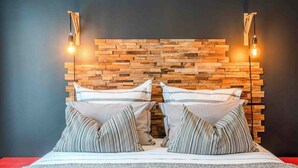 Una cama con cabecera de madera, dos lámparas de noche y almohadas a rayas.
