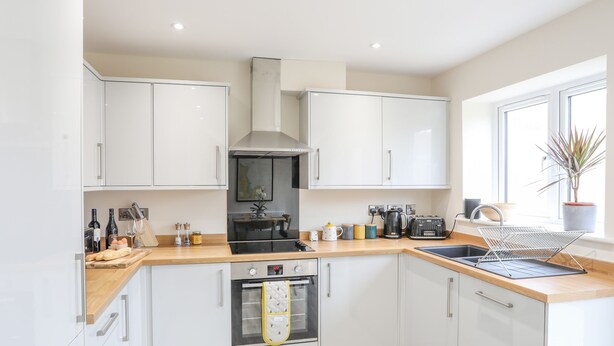 A modern kitchen with white cabinets, a black oven, and a wooden countertop. - Swn Y Nant (Holyhead)
