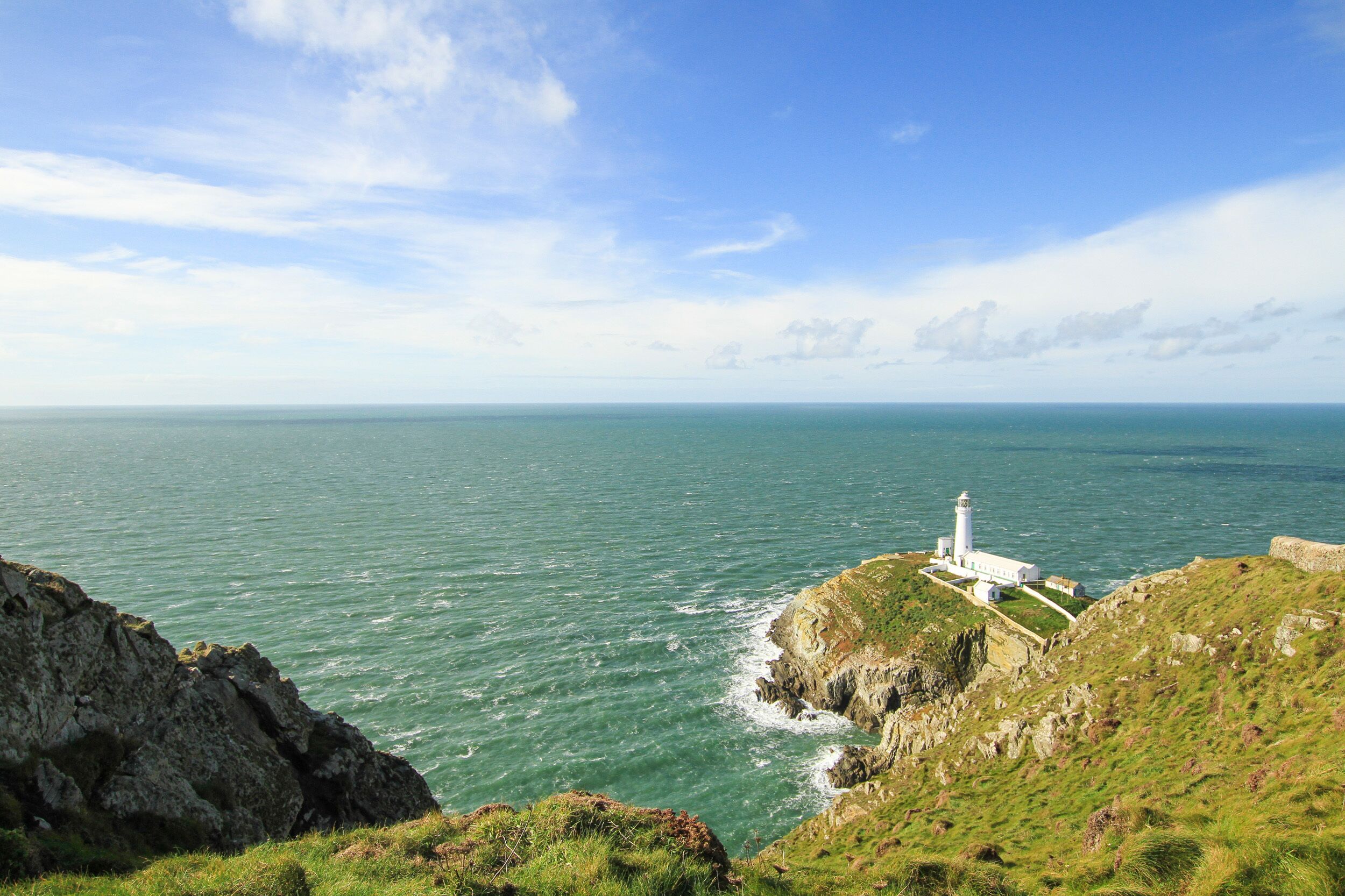 A coastal view with a lighthouse on a grassy cliff overlooking the sea.
