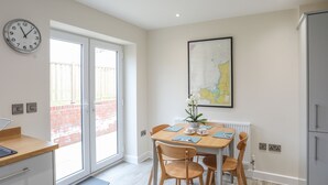 A modern kitchen with a dining area, a large window, and a wall-mounted clock. - Swn Y Nant (Holyhead)