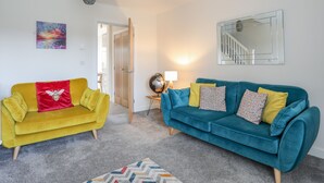 A living room with a yellow sofa, a teal sofa, a globe, and a painting on the wall. - Swn Y Nant (Holyhead)