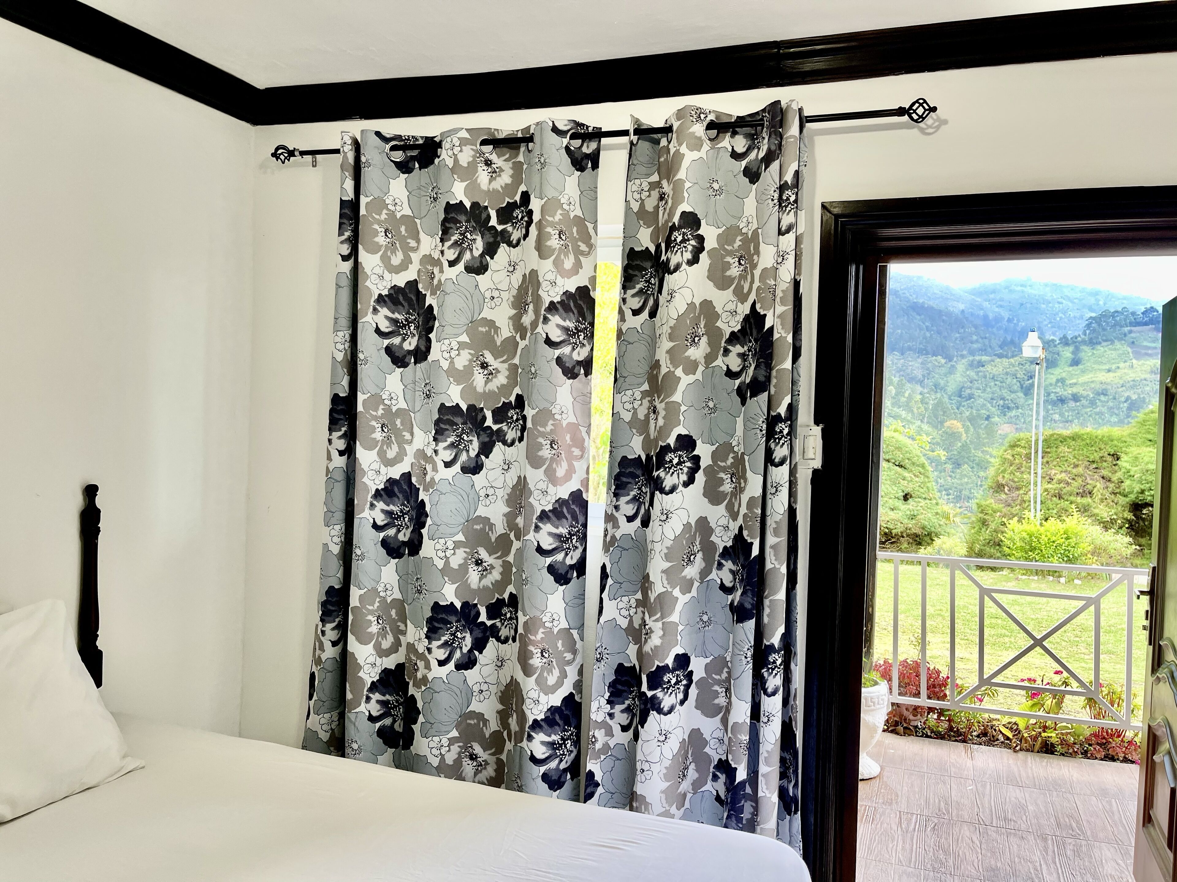 A bedroom with a bed, floral curtains, and a view of a balcony with greenery.
