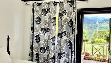 A bedroom with a bed, floral curtains, and a view of a balcony with greenery.