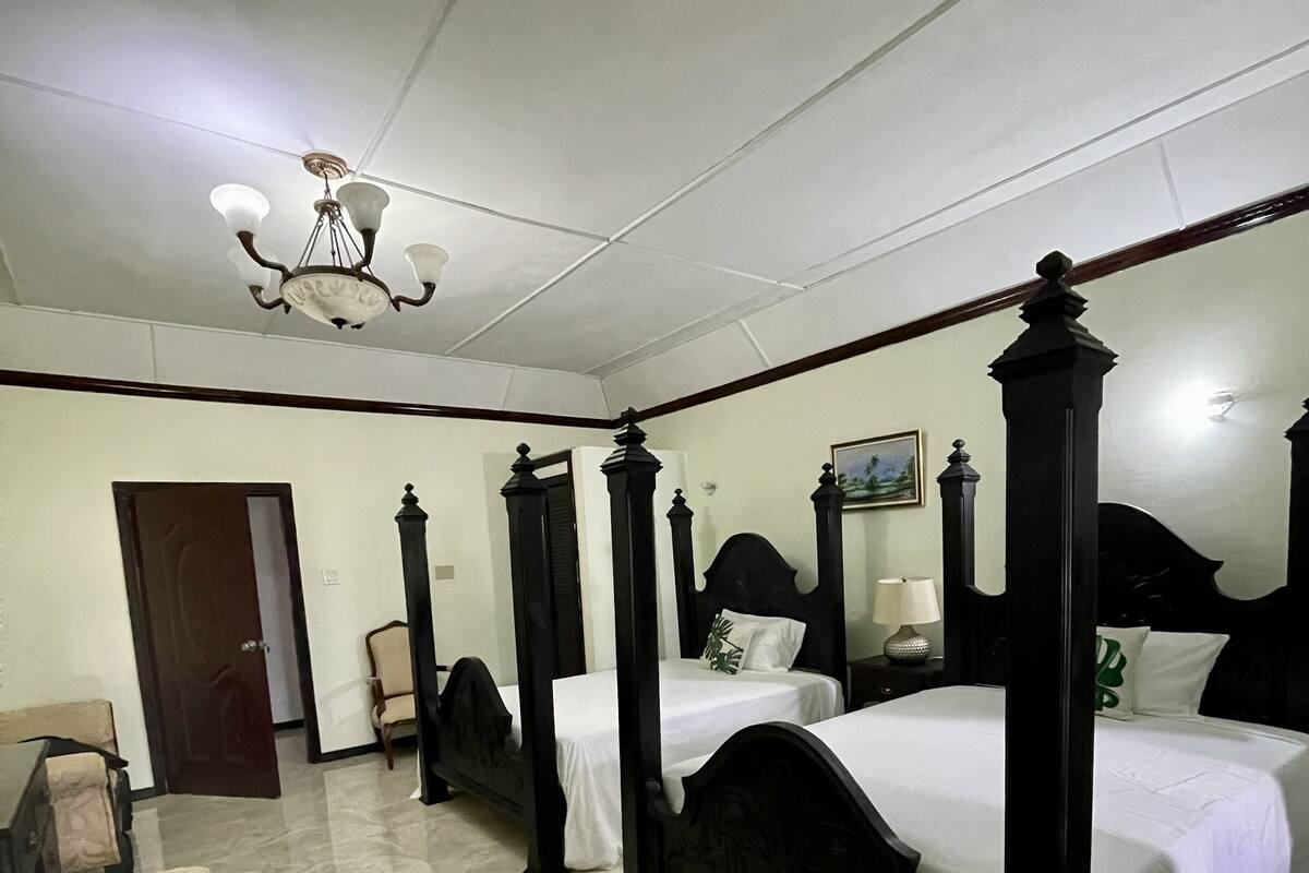 Una cama con dosel, ropa de cama blanca, una silla de madera y una mesita de noche con una lámpara.