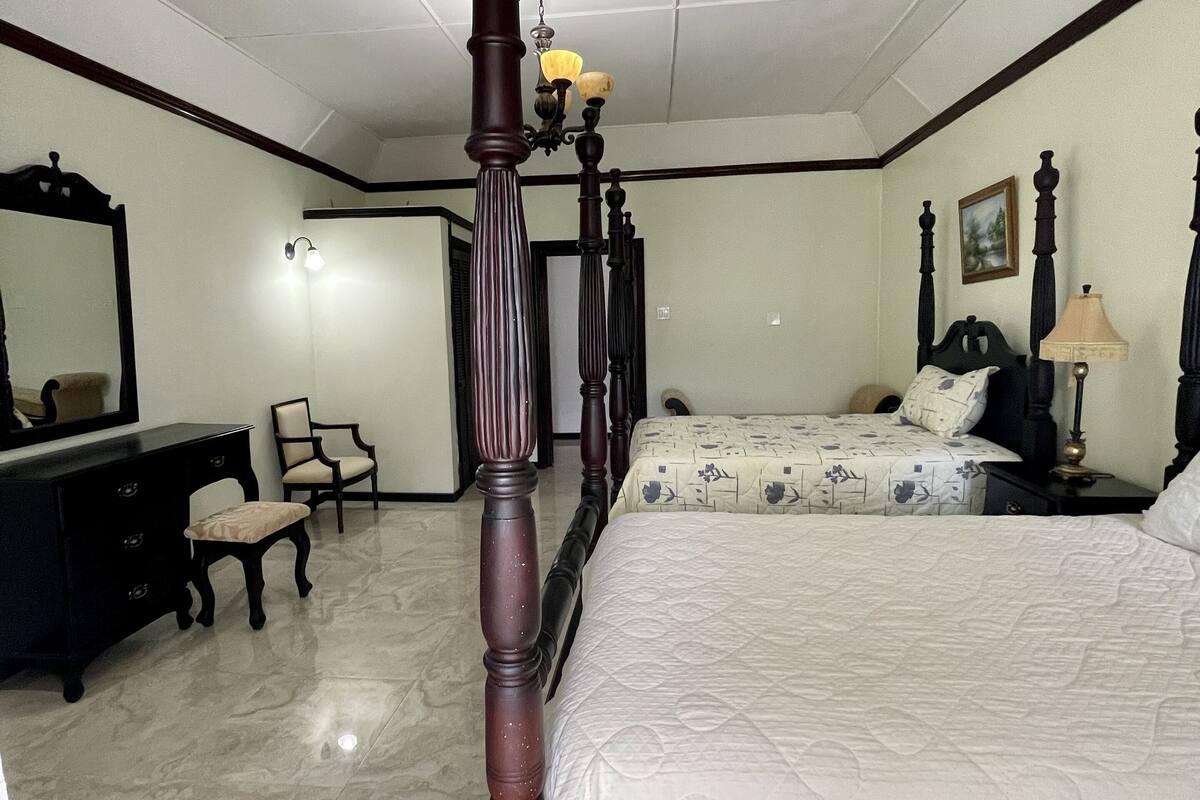 Un dormitorio con cama con dosel, cómoda, silla y mesita de noche con lámpara.