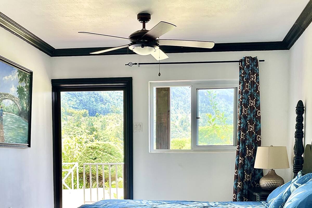 Un dormitorio con cama, ventilador de techo, ventana y puerta que da a un balcón.