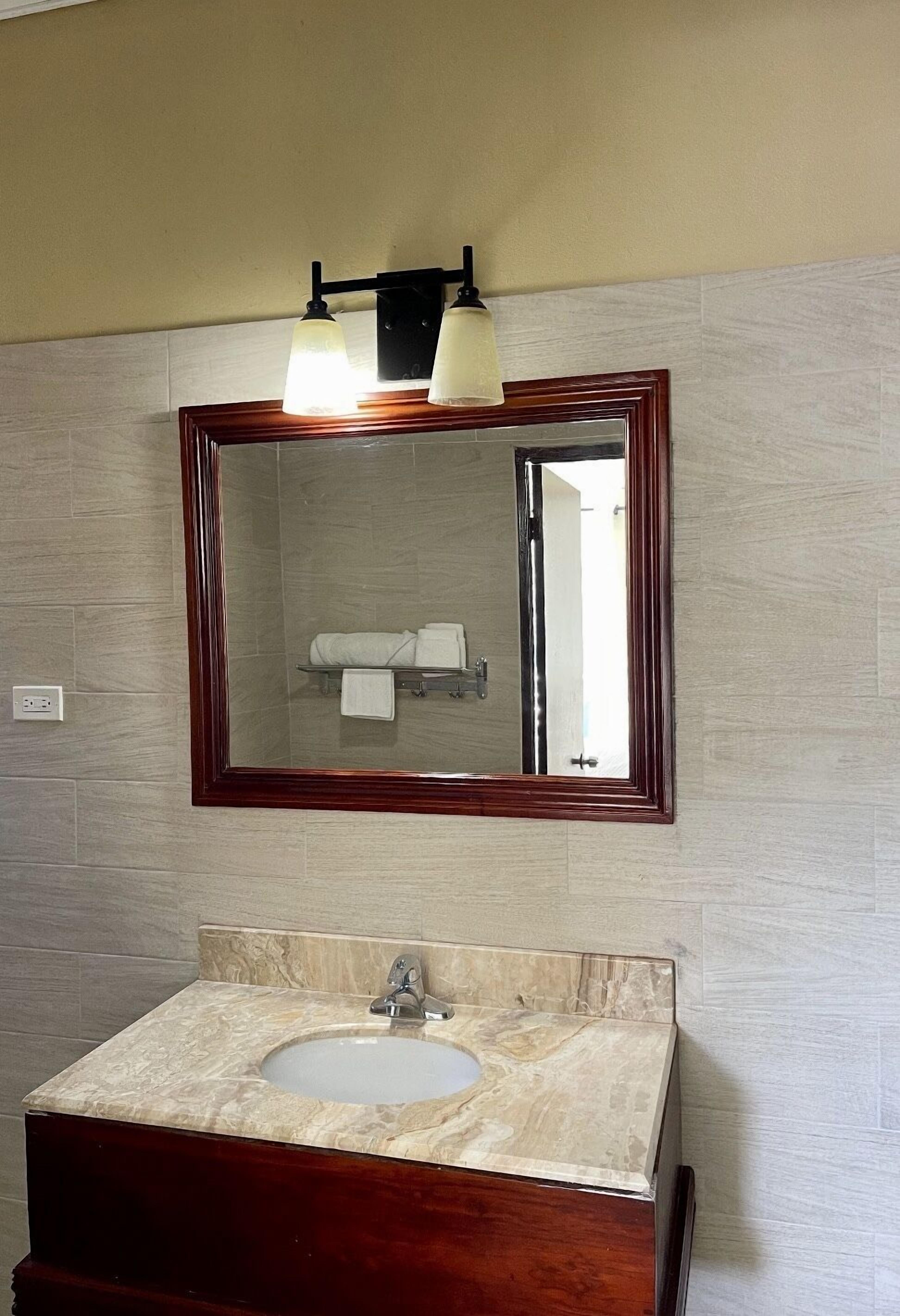 Un baño con lavamanos de mármol, tocador de madera, un espejo grande con marco de madera y un perchero sobre el espejo.