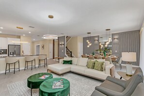 Un salon moderne avec un canapé d’angle, un coin repas et une cuisine en arrière-plan.