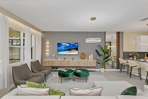 Un salon moderne doté d’un grand téléviseur, de sièges confortables, d’un coin cuisine et d’un espace repas.