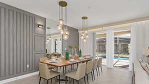 A modern dining area with a wooden table set for six, surrounded by chairs. There is a large mirror on the wall, and a hanging light fixture above the table. - Last Minute Disney Getaway! Luxury Villa with Private Pool. Book Now! #39946 (Orlando)