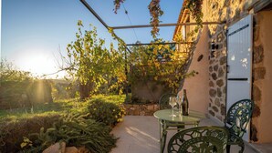 An outdoor patio with a stone wall, a glass table, and metal chairs. - Cosy ALL NEW cottage with swimming pool- (Tanneron)