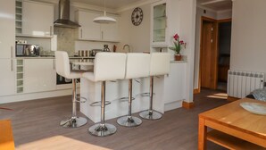 Una cocina moderna con armarios blancos, una campana extractora de acero inoxidable y una zona de comedor con taburetes blancos.