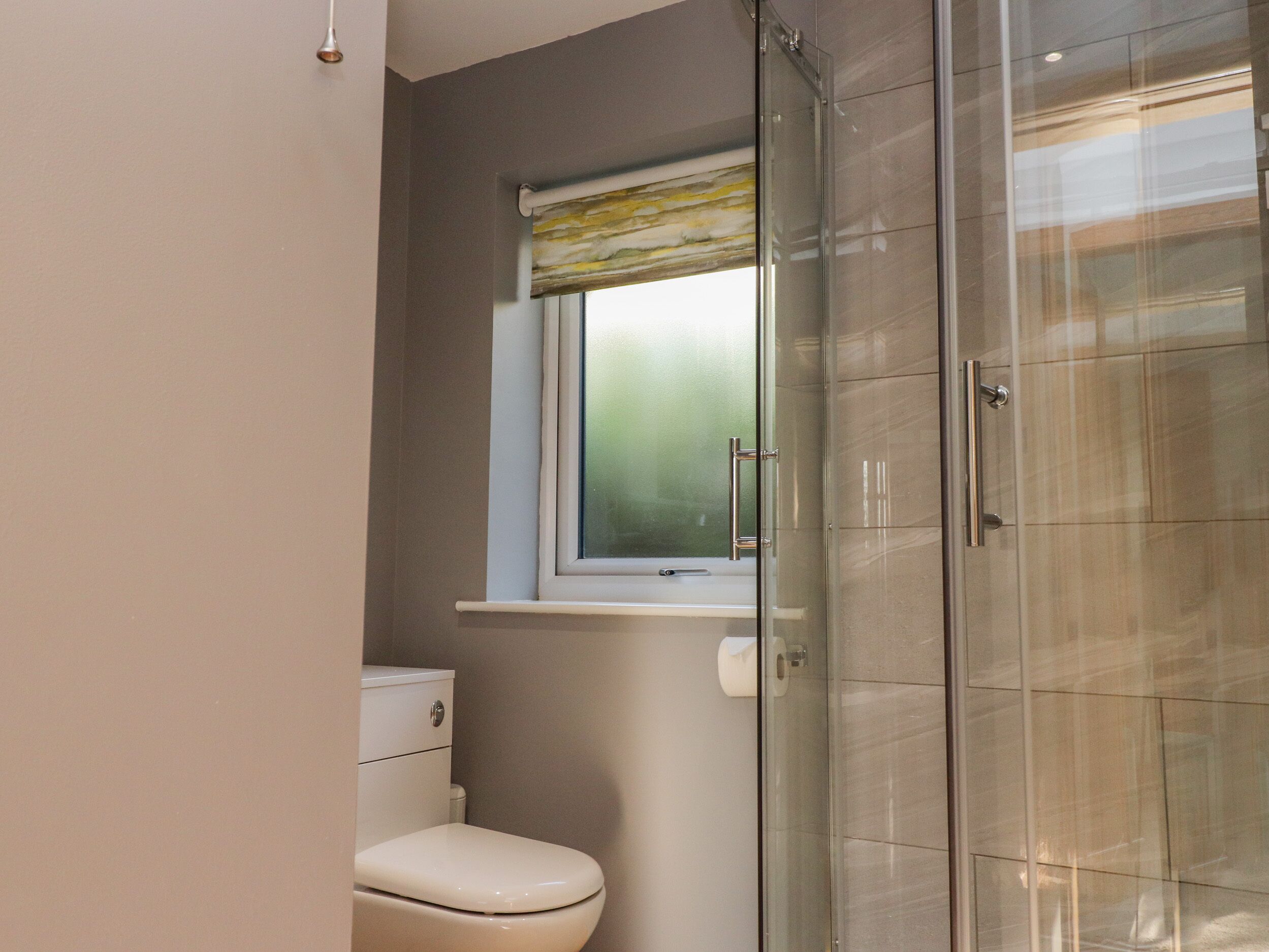 Un baño moderno con inodoro, cabina de ducha de vidrio y ventana con panel esmerilado.