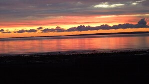 Un coucher de soleil sur une étendue d'eau calme, avec une côte visible au loin.