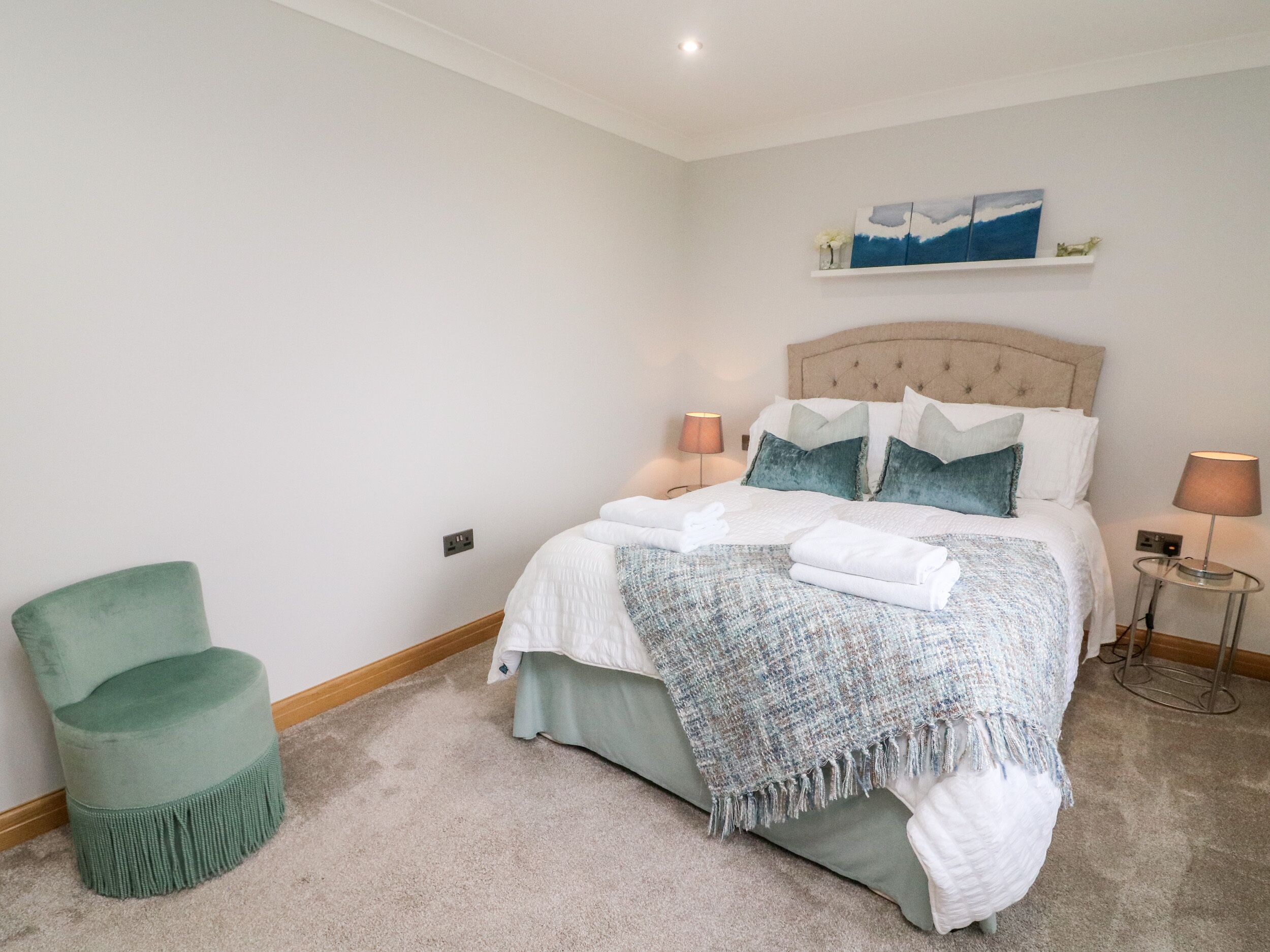 A neatly arranged bedroom with a bed, bedside lamps, a chair, and a painting on the wall.