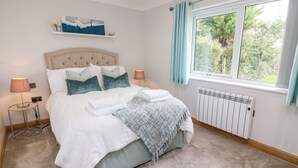 Un lit bien fait, avec des oreillers et une couverture, une lampe de chevet, un radiateur et une fenêtre avec des rideaux.