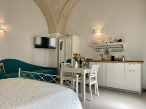 Een kleine slaapkamer met een bed, bureau en kitchenette.