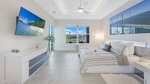 Een moderne slaapkamer met een groot bed, een aan de muur bevestigde televisie en uitzicht op het buitenleven door een raam.