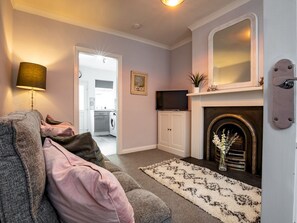 A living room with a sofa, a fireplace, a television, and a kitchen in the background.