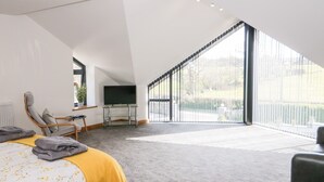 Une chambre moderne avec une grande fenêtre, un lit recouvert d’une couvre-lit à motifs floraux, une chaise et un téléviseur posé sur un meuble.